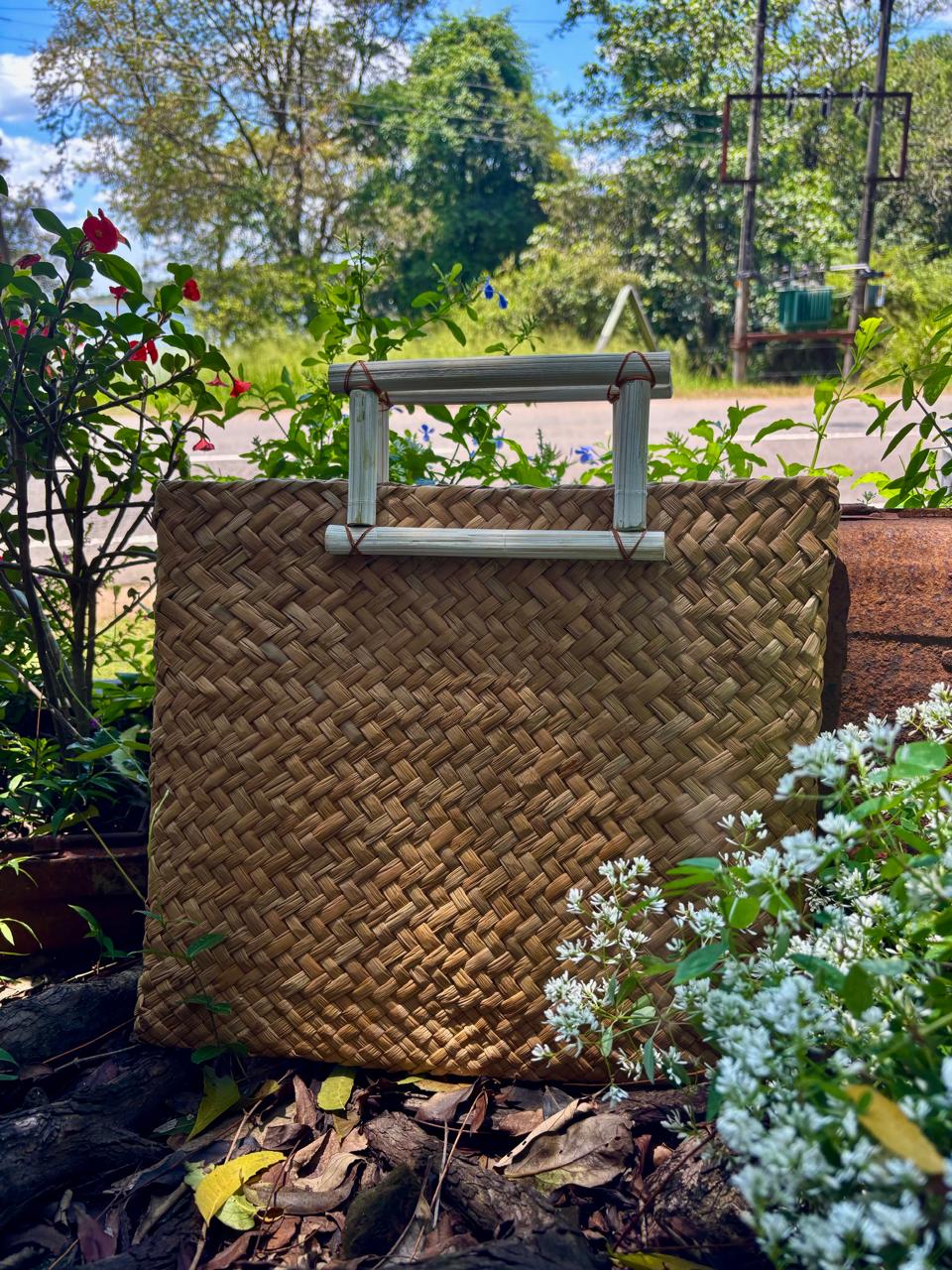 A handwoven straw bag with bamboo handles, displayed among garden flowers at Hambu Café